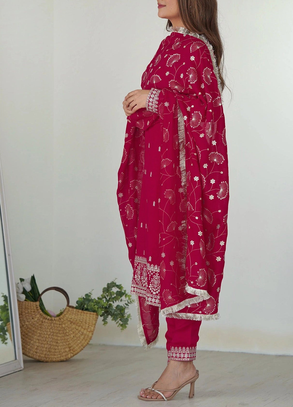 Woman wearing a pink traditional outfit with white patterns, standing against a plain background.